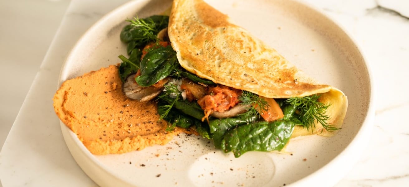 vegetable filled omelette on a round cream color plate matching the background corner of the table